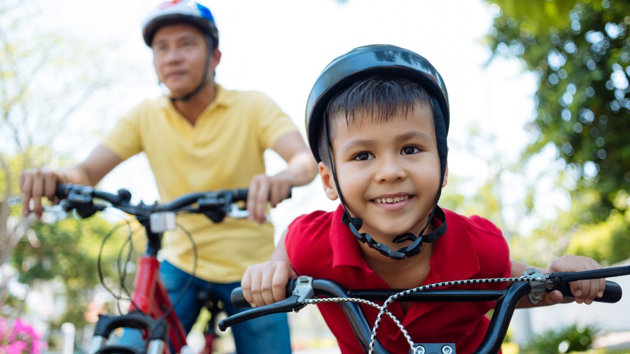 Happy mixed-race boy and his father cycling in the park